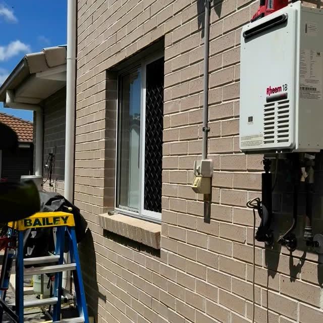 External electric hot water system mounted beside residential brick wall.
