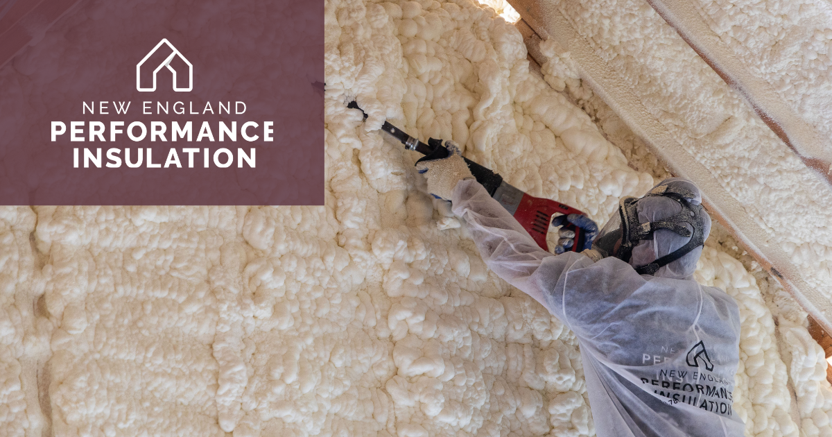 A person in protective gear uses a spray foam gun to apply insulation to the interior wall and rafters of a building.