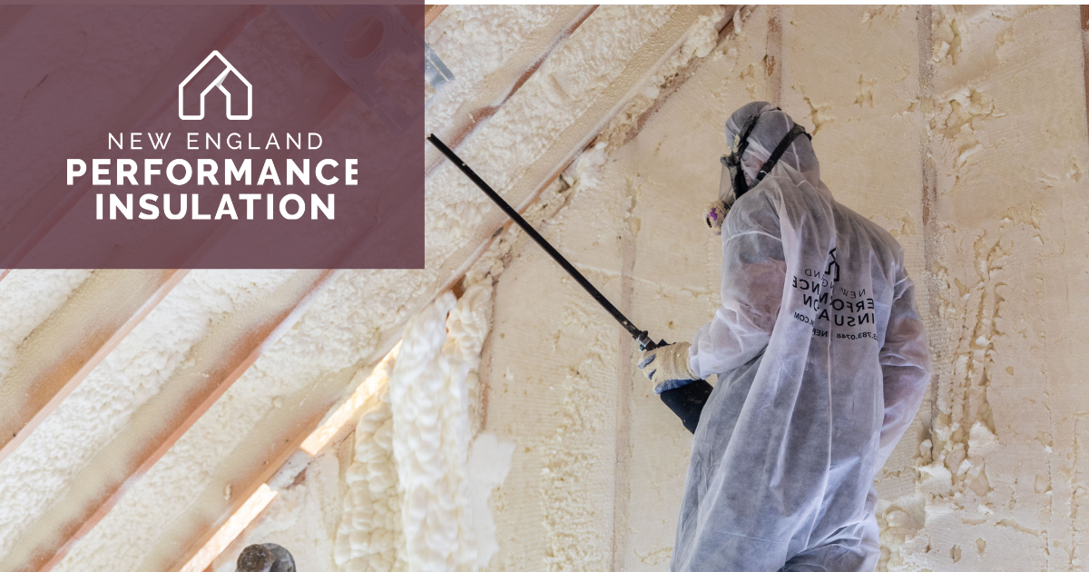 A worker in protective gear sprays foam insulation onto the wooden rafters and walls of an attic interior.