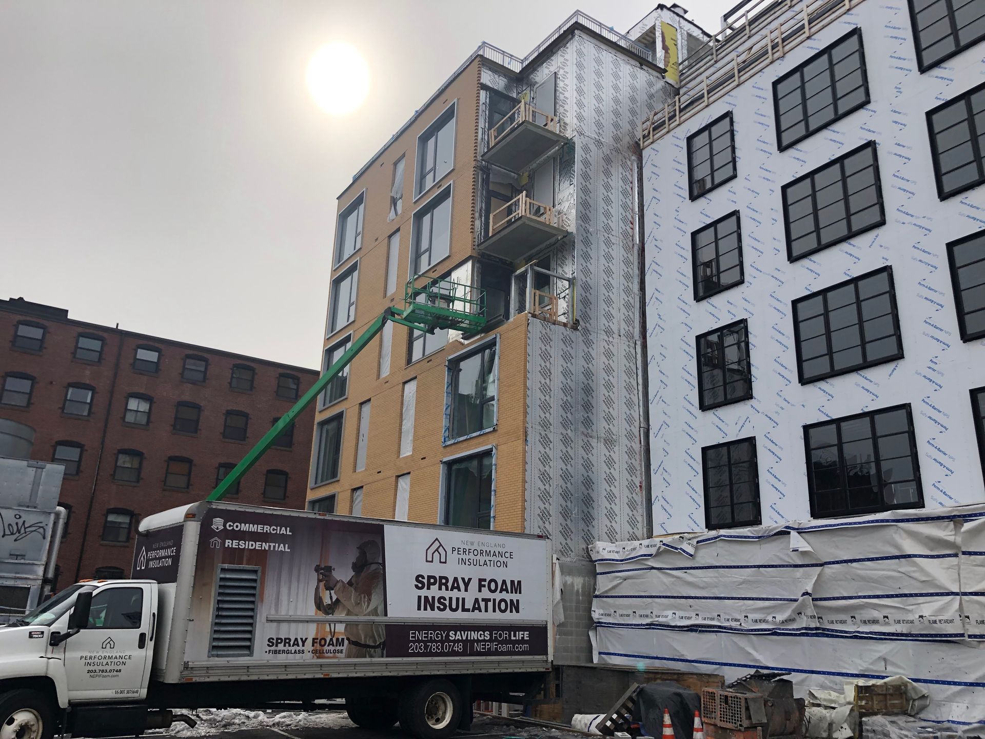 Construction site: workers insulating a modern building with a spray foam truck.