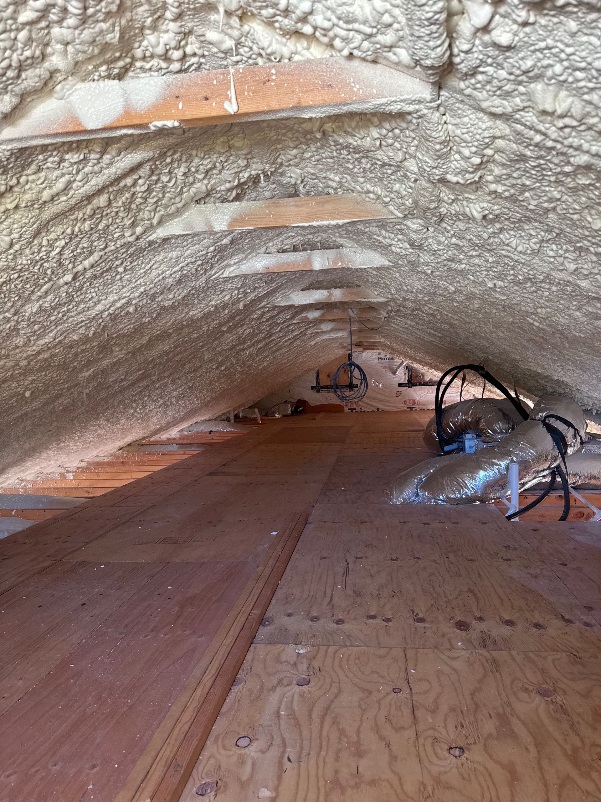 Attic with spray foam insulation on the walls and roof. Wooden floorboards.