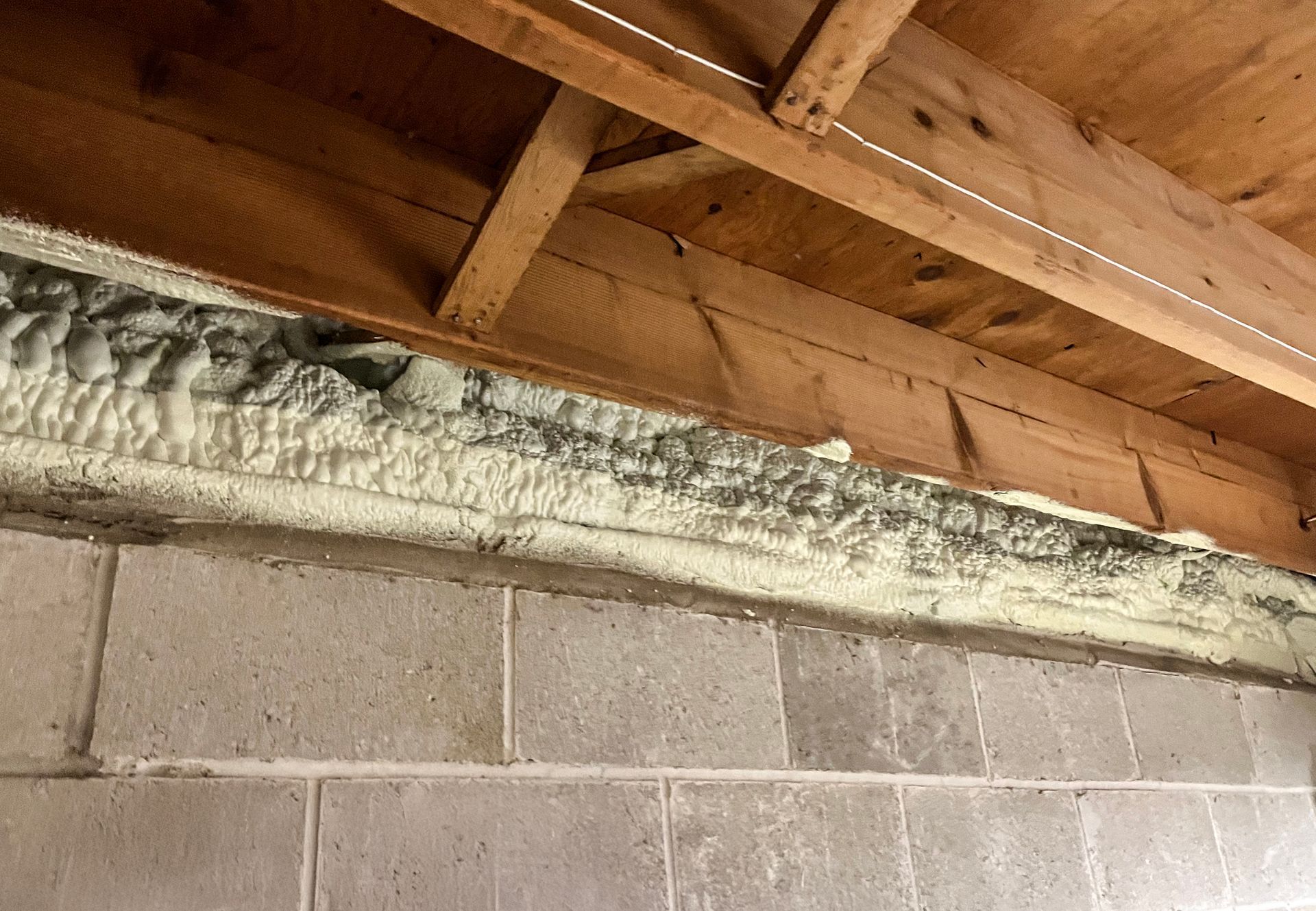 A rim joist with a lot of foam on it and a block foundation.