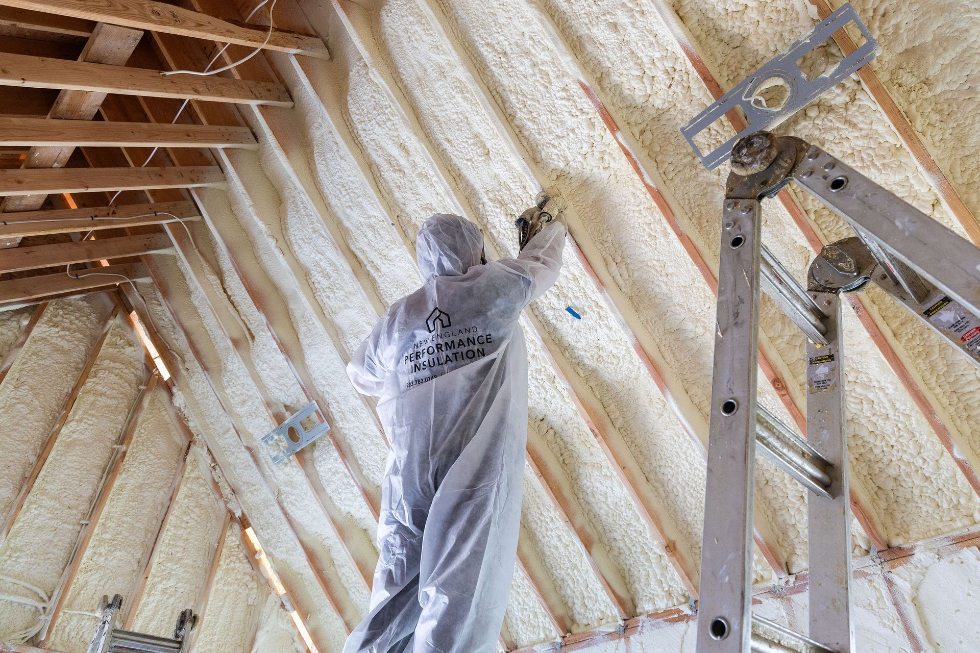 A man in a protective suit is spraying foam on the ceiling of a building.