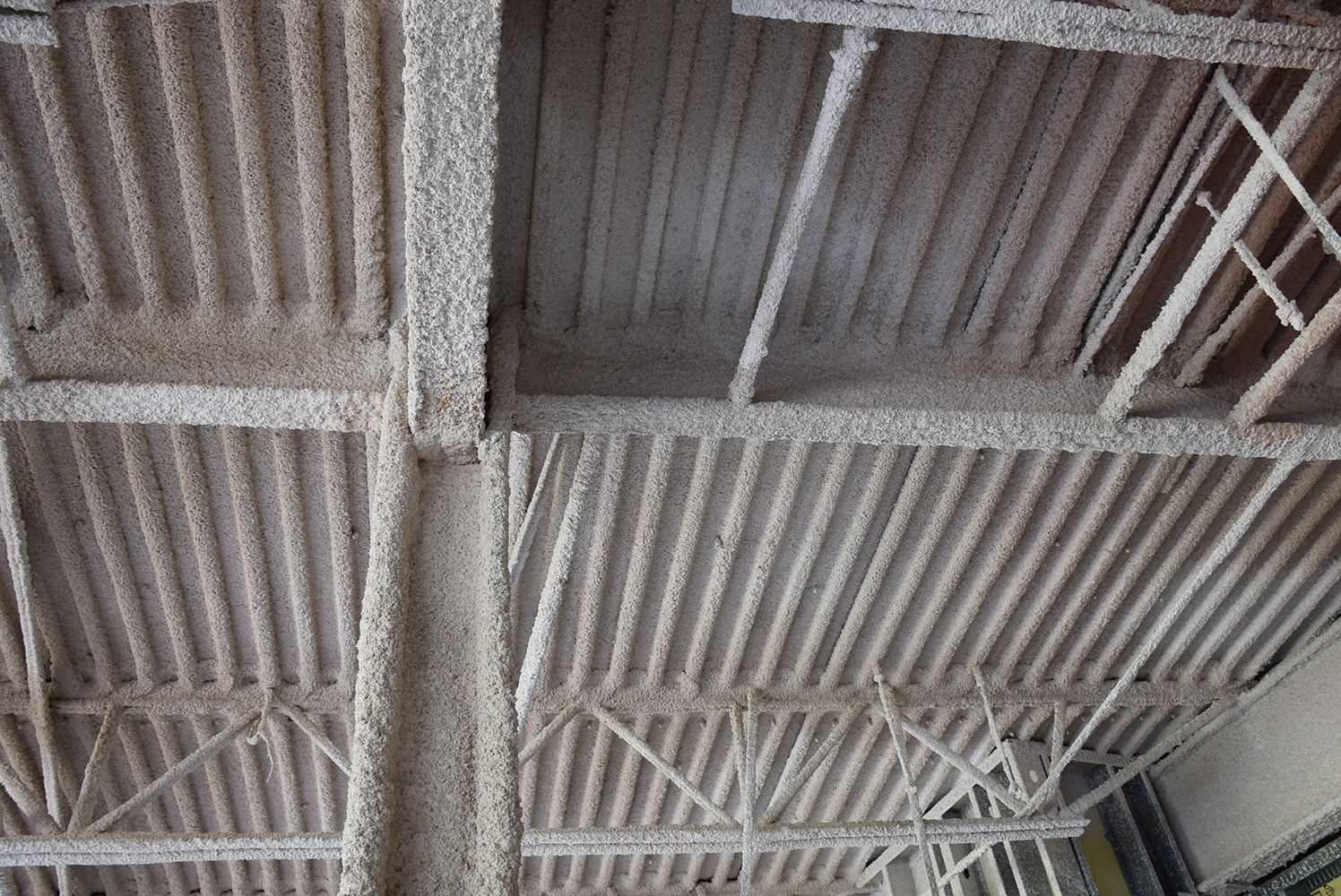The metal ceiling of a building with a lot of fireproofing on it.