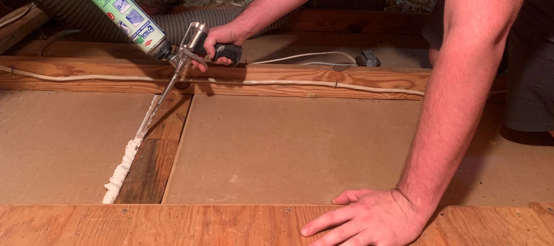 A person is spraying foam into a hole in the floor of an attic.
