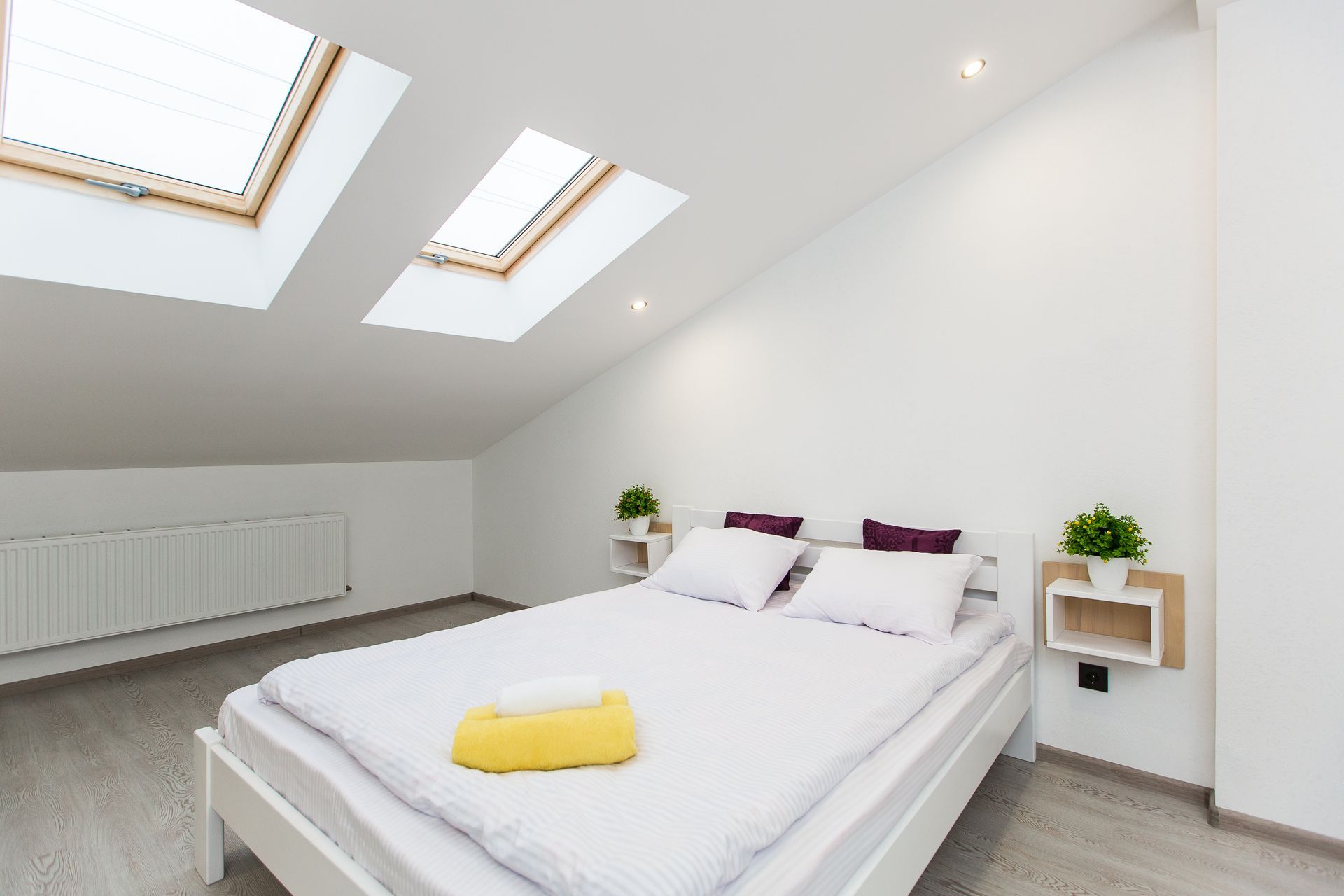 Bedroom with a bed, skylights, and built-in shelves; white walls and light gray flooring.