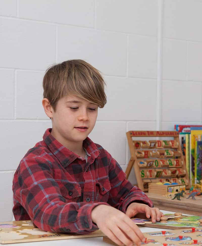 A Young Boy Is Sitting at A Table Playing with A Puzzle — Sunshine Coast Financial Advisers in Maroochydore, QLD