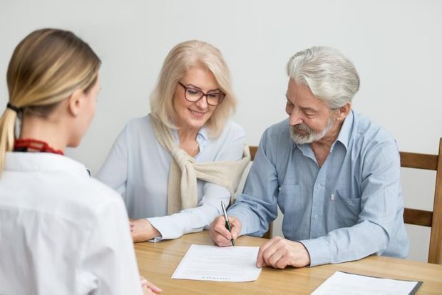 An Elderly Couple Is Signing a Document While Sitting at A Table with A Doctor — Sunshine Coast Financial Advisers in Maroochydore, QLD