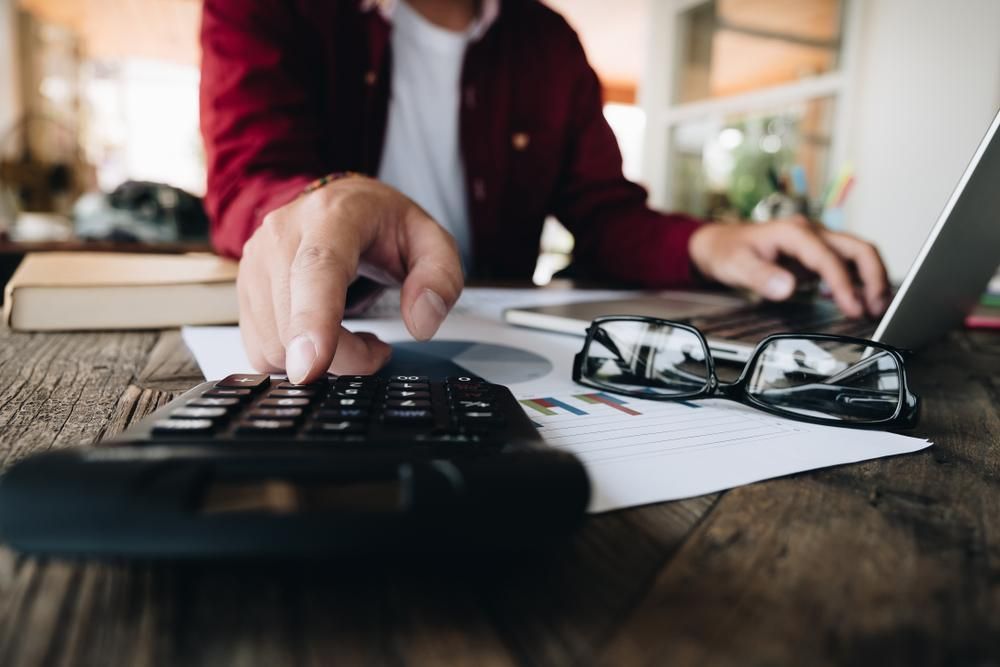 A Man Is Using a Laptop and A Calculator at The Same Time — Sunshine Coast Financial Advisers in Maroochydore, QLD