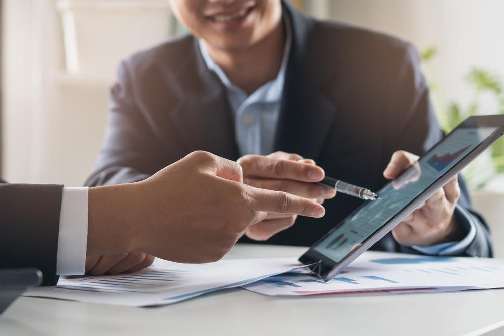 Two Men Are Sitting at A Table Looking at A Tablet — Sunshine Coast Financial Advisers in Maroochydore, QLD