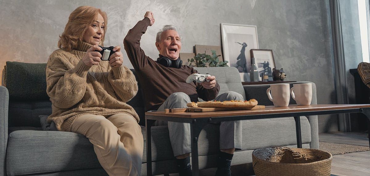 An Elderly Couple Is Sitting on A Couch Playing a Video Game — Sunshine Coast Financial Advisers in Maroochydore, QLD