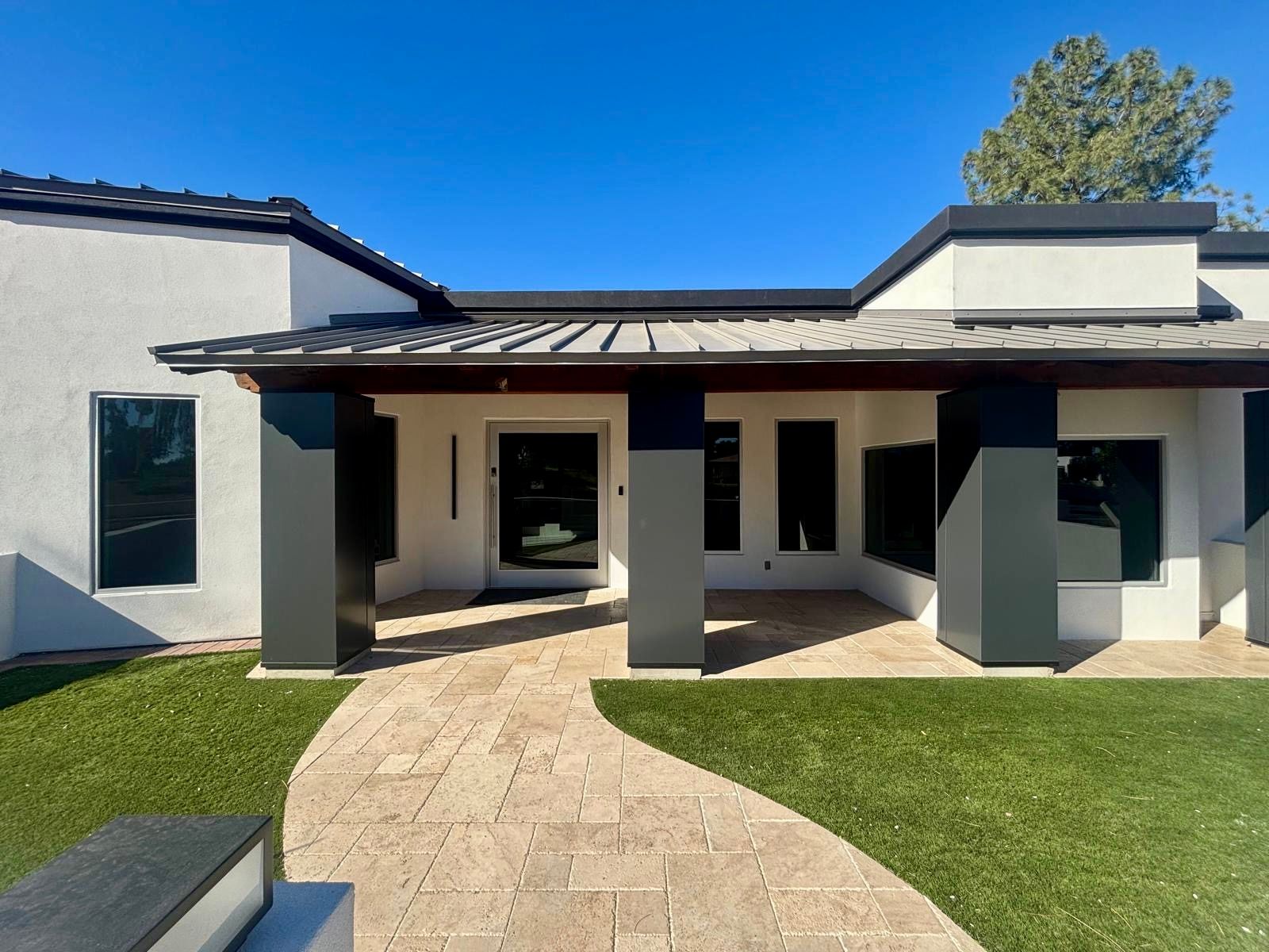 Modern white house with dark accents, porch, and a stone walkway. Green grass and blue sky.