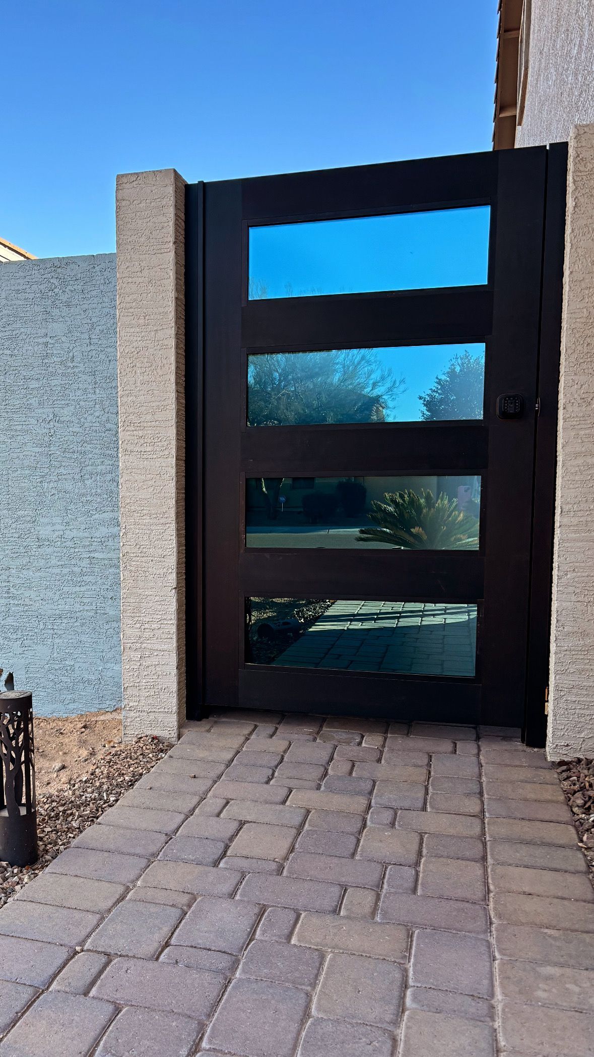 Black door with four glass panels set into a beige stone wall with a brick pathway.