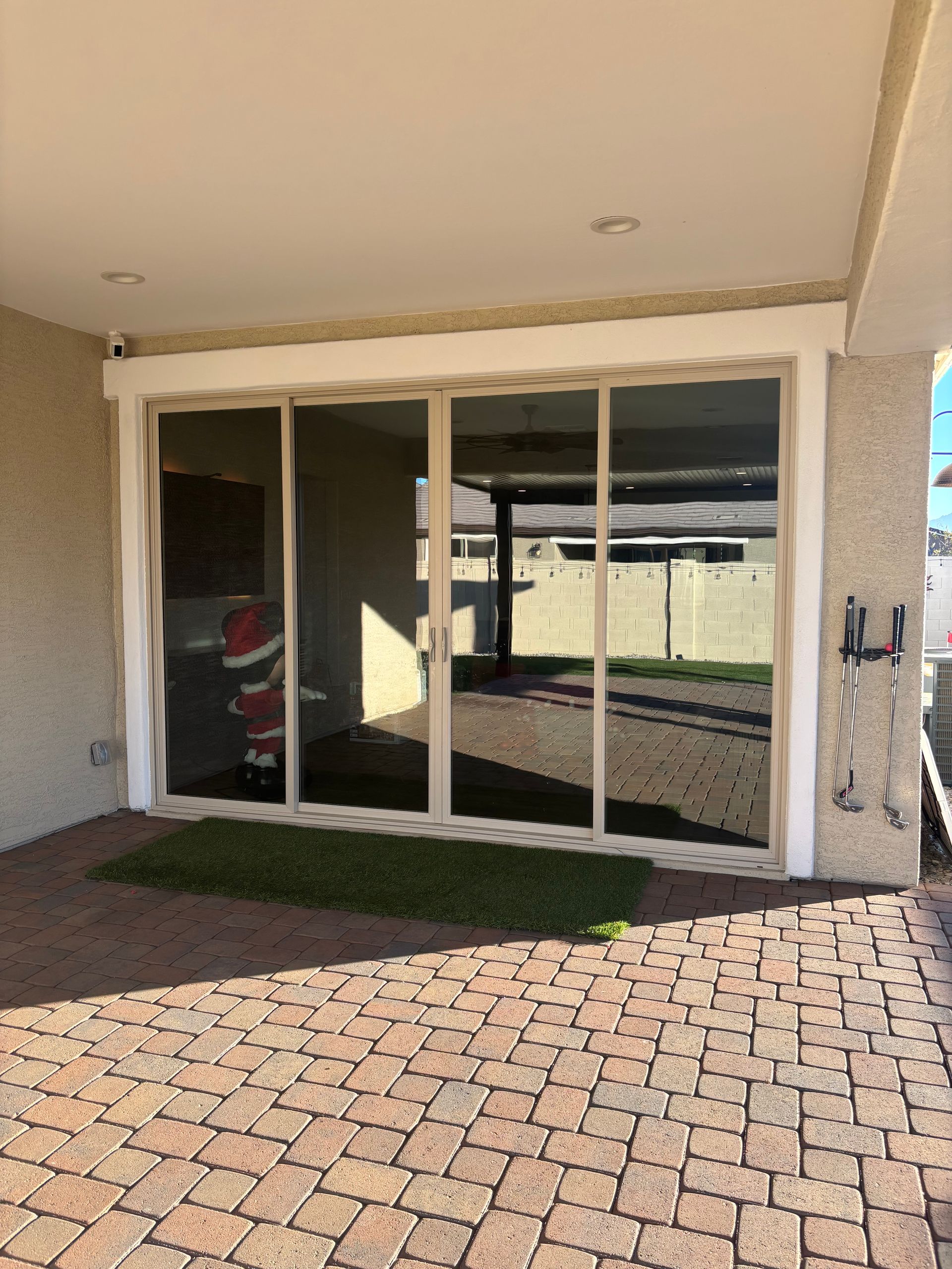 Sliding glass doors on a patio with brick flooring, under a beige-colored overhang.