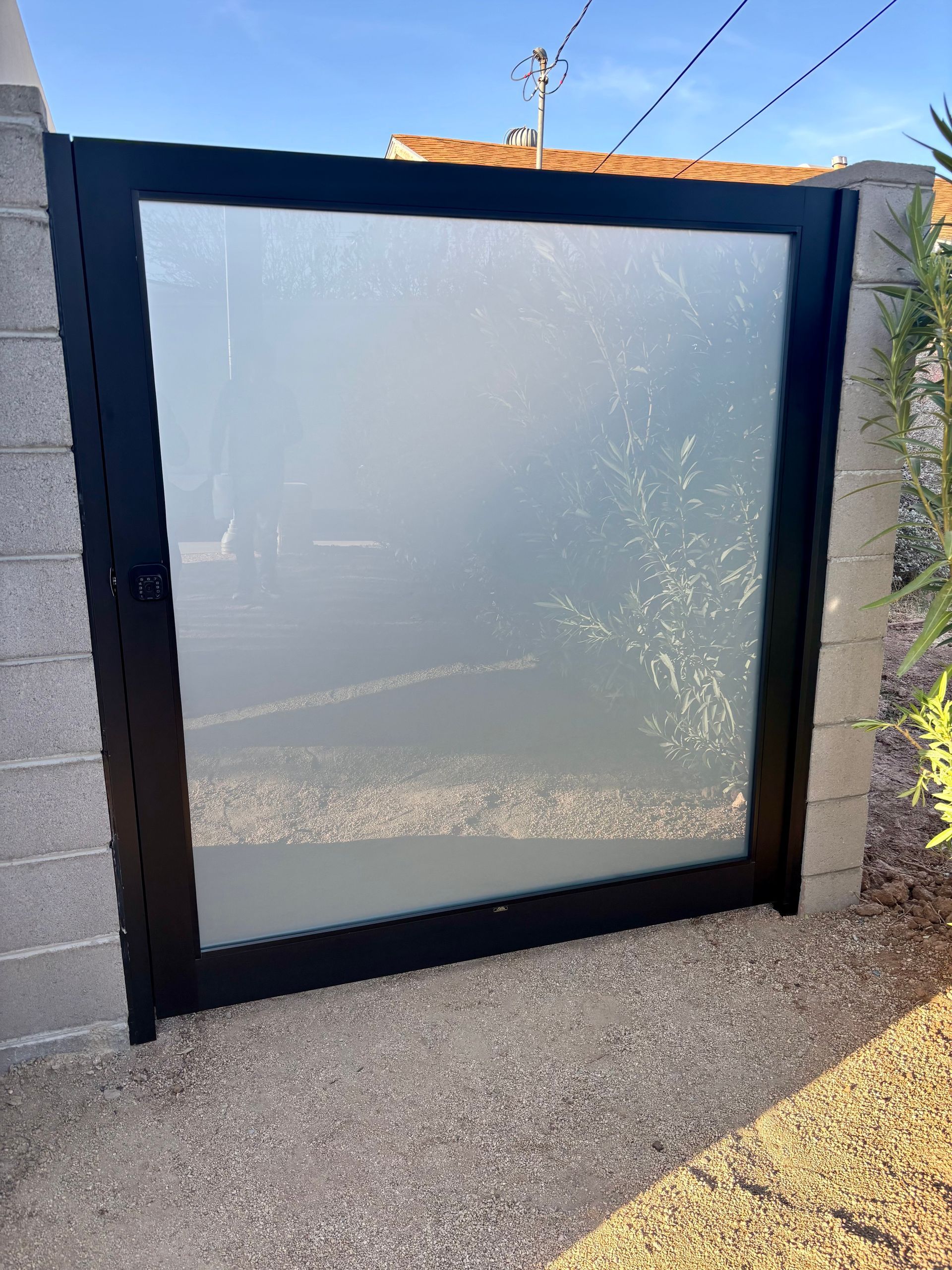 Black metal gate with frosted glass panel set in cinder block pillars.