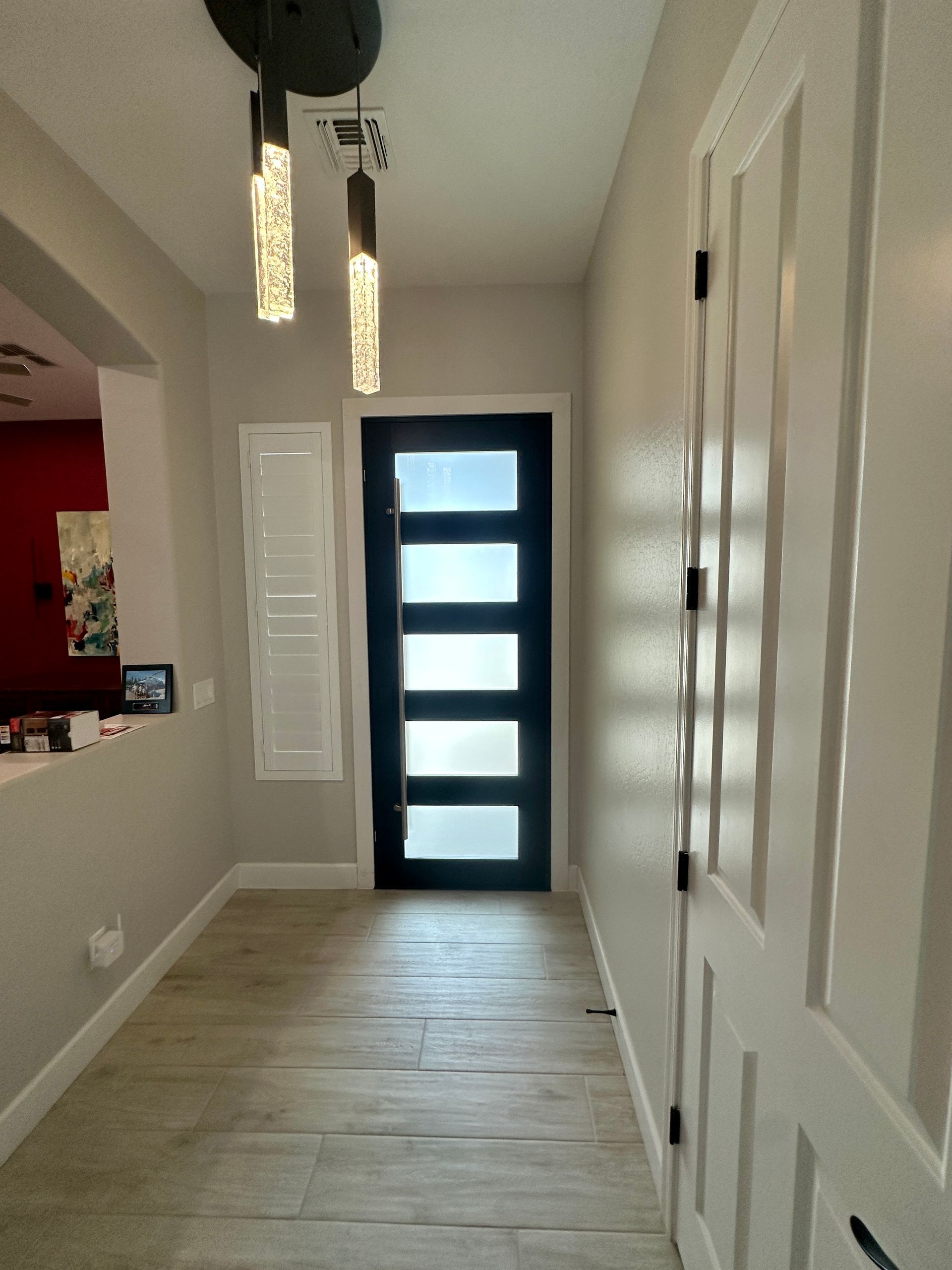 Hallway with wood-look tile, light gray walls, black front door with glass panels, and modern light fixtures.