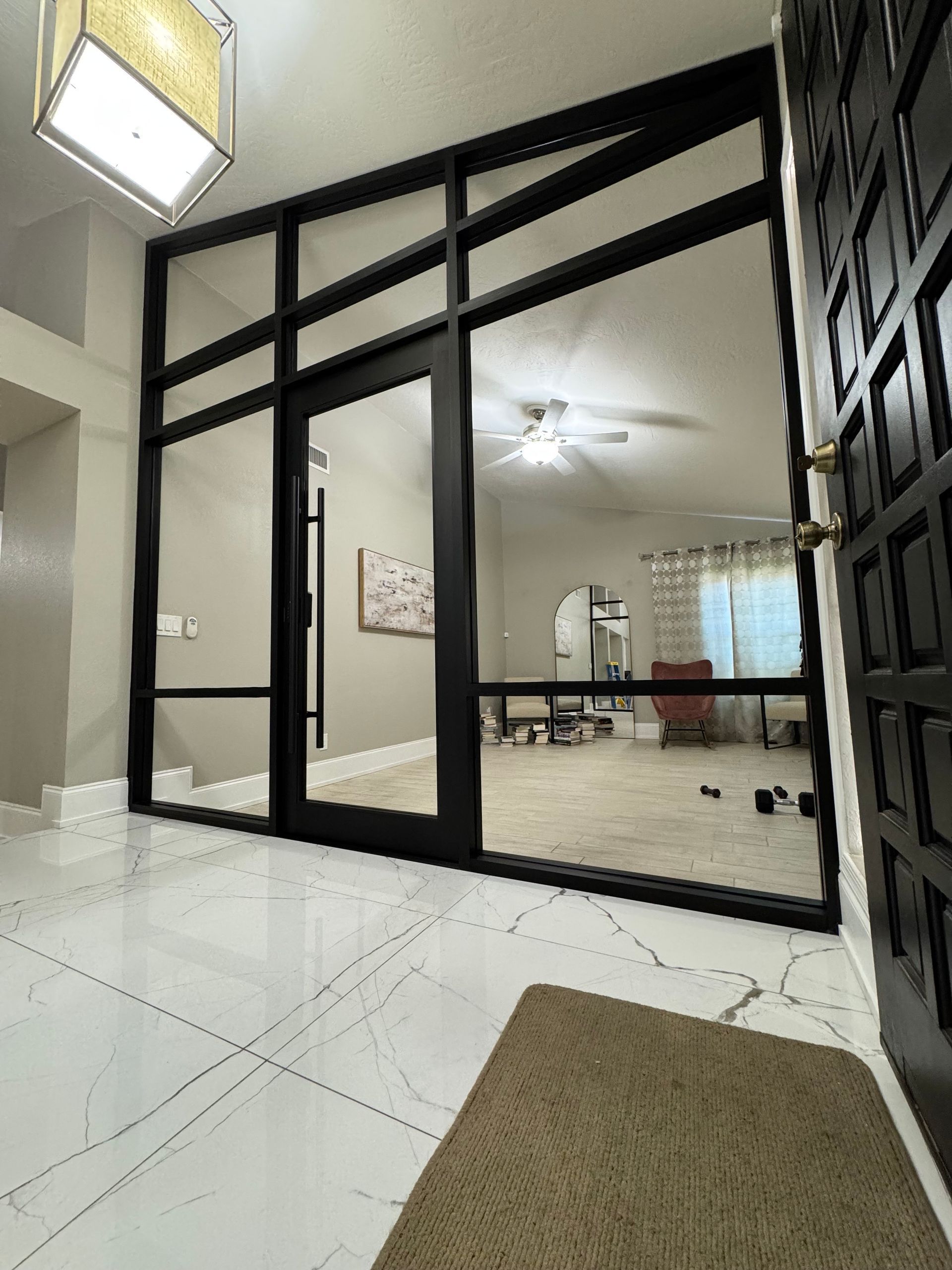 Entryway with black-framed glass doors and windows. Brown doormat on white tiled floor. Interior view with furniture.