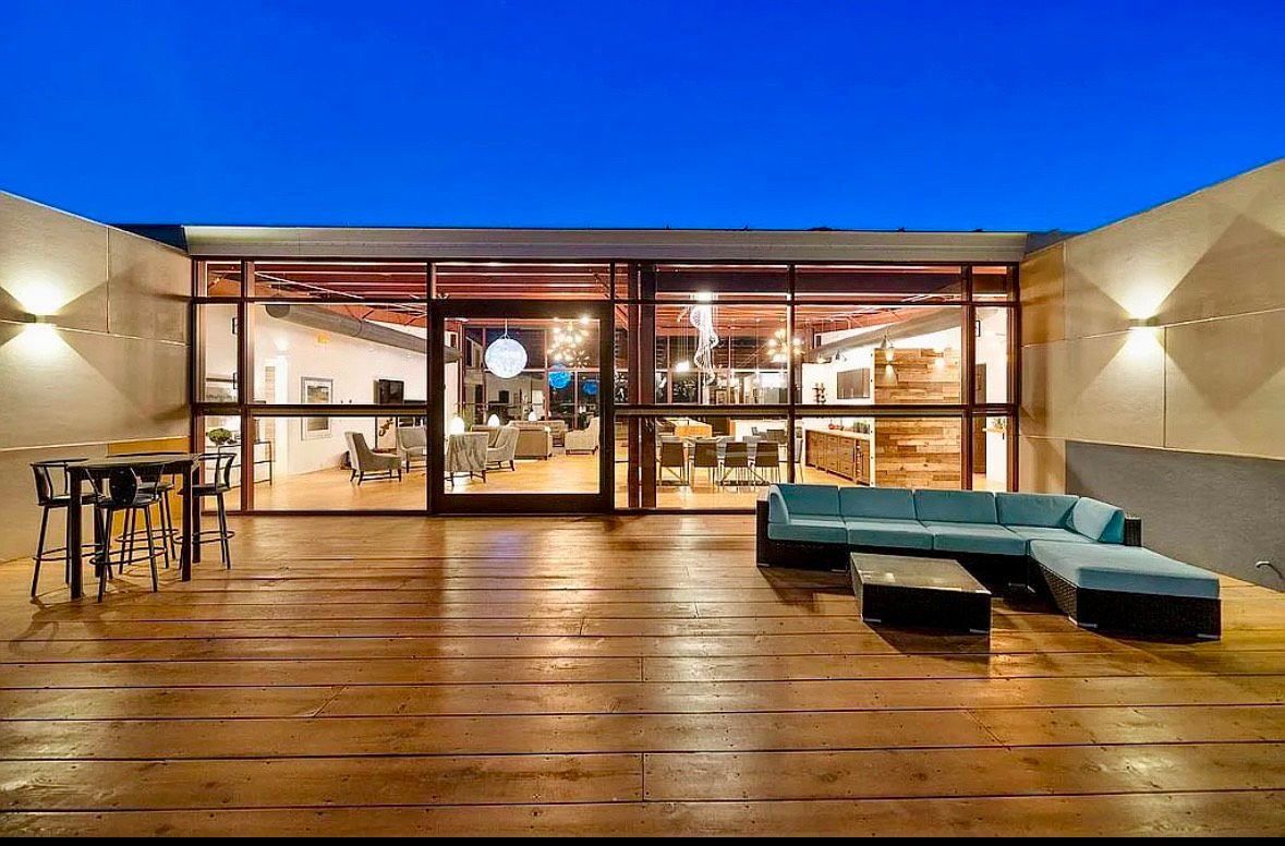 Rooftop patio with turquoise sectional sofa, wooden floor, and glass-walled building at dusk.