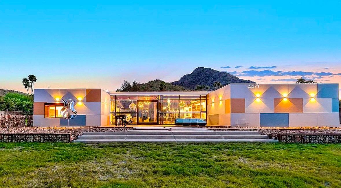 Modern house with glass walls and colorful facade, set against a mountain and dusk sky.
