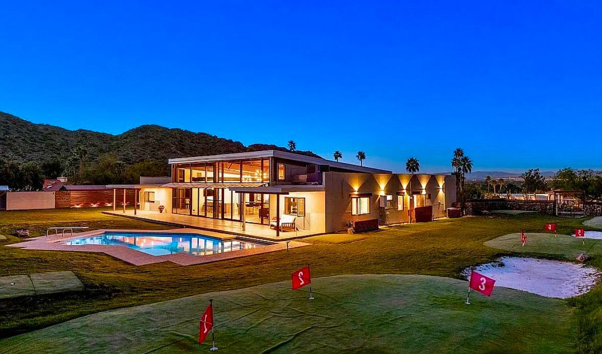 Modern house with a pool and small golf course in front, under a clear blue sky.