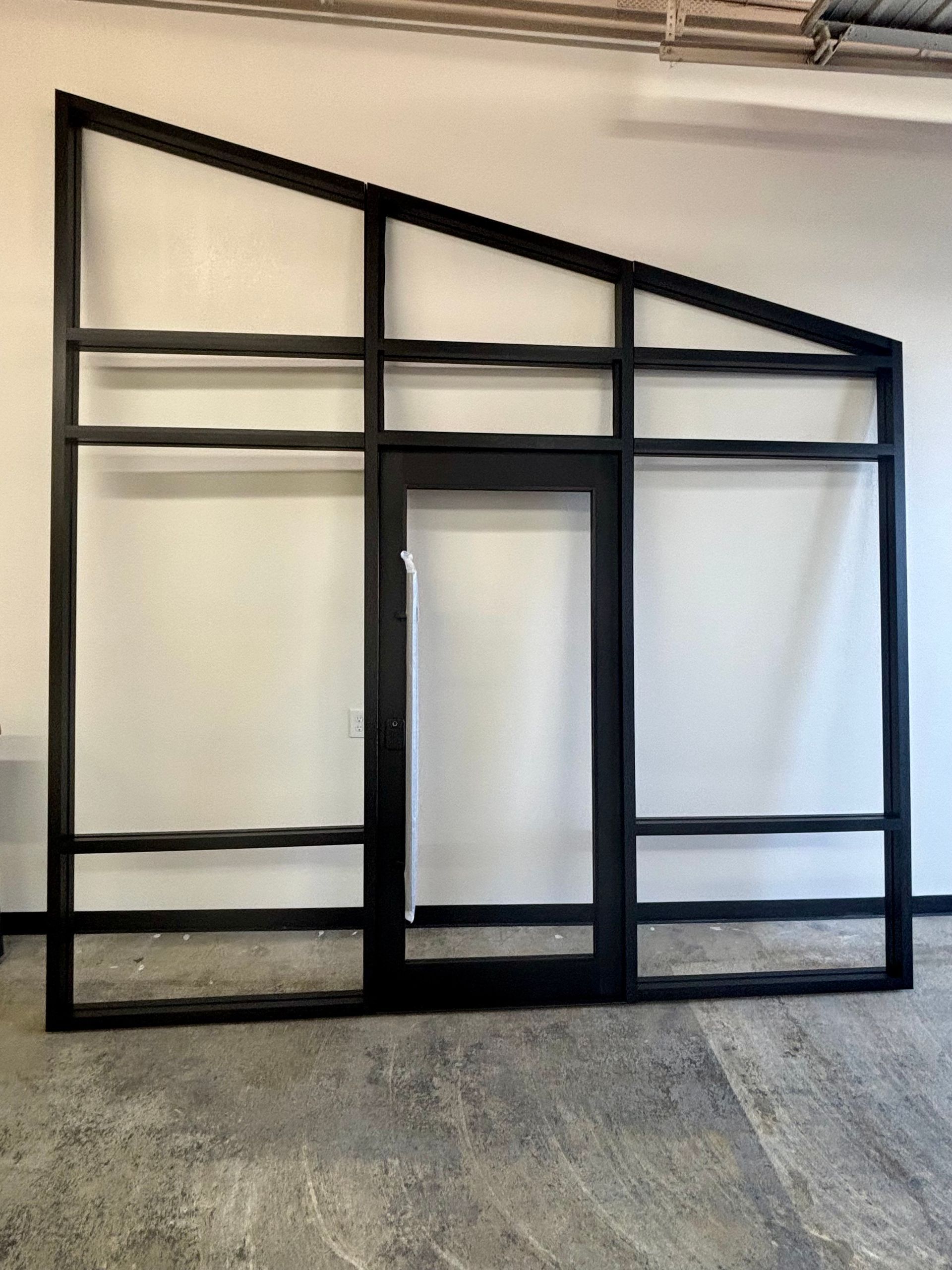 Black metal frame with a door and angled top section, against a white wall.