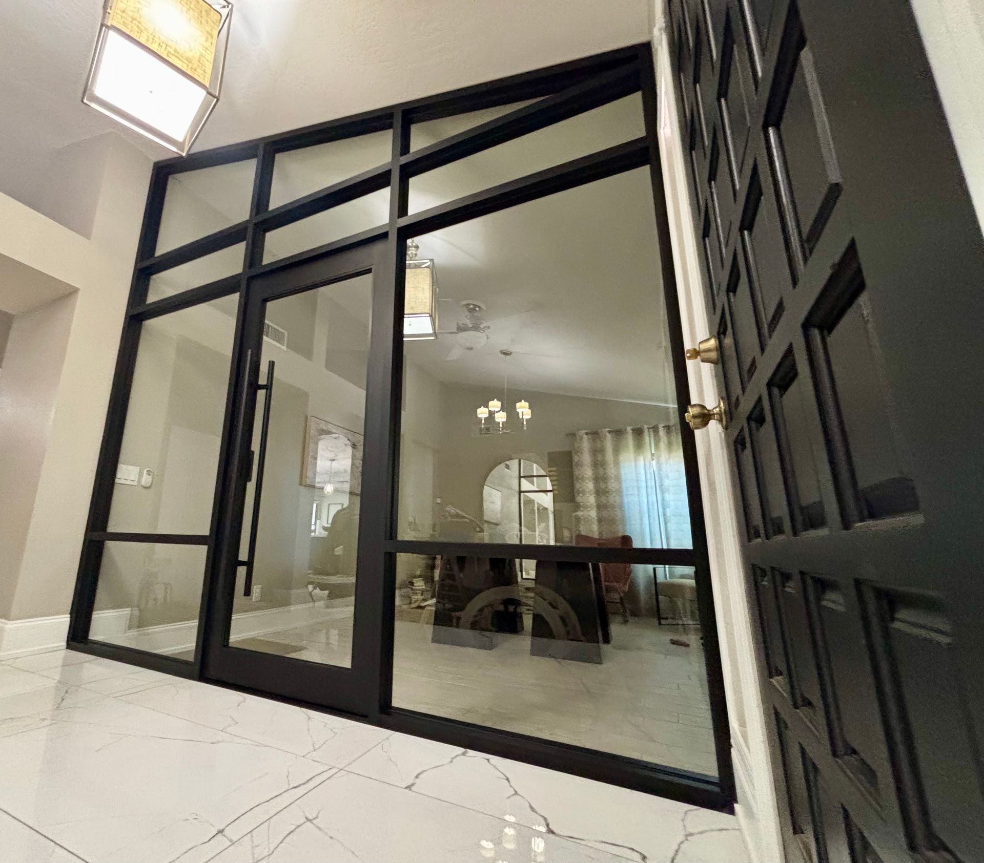 Black framed glass entry door and sidelights. White tile floor. Interior view through glass.