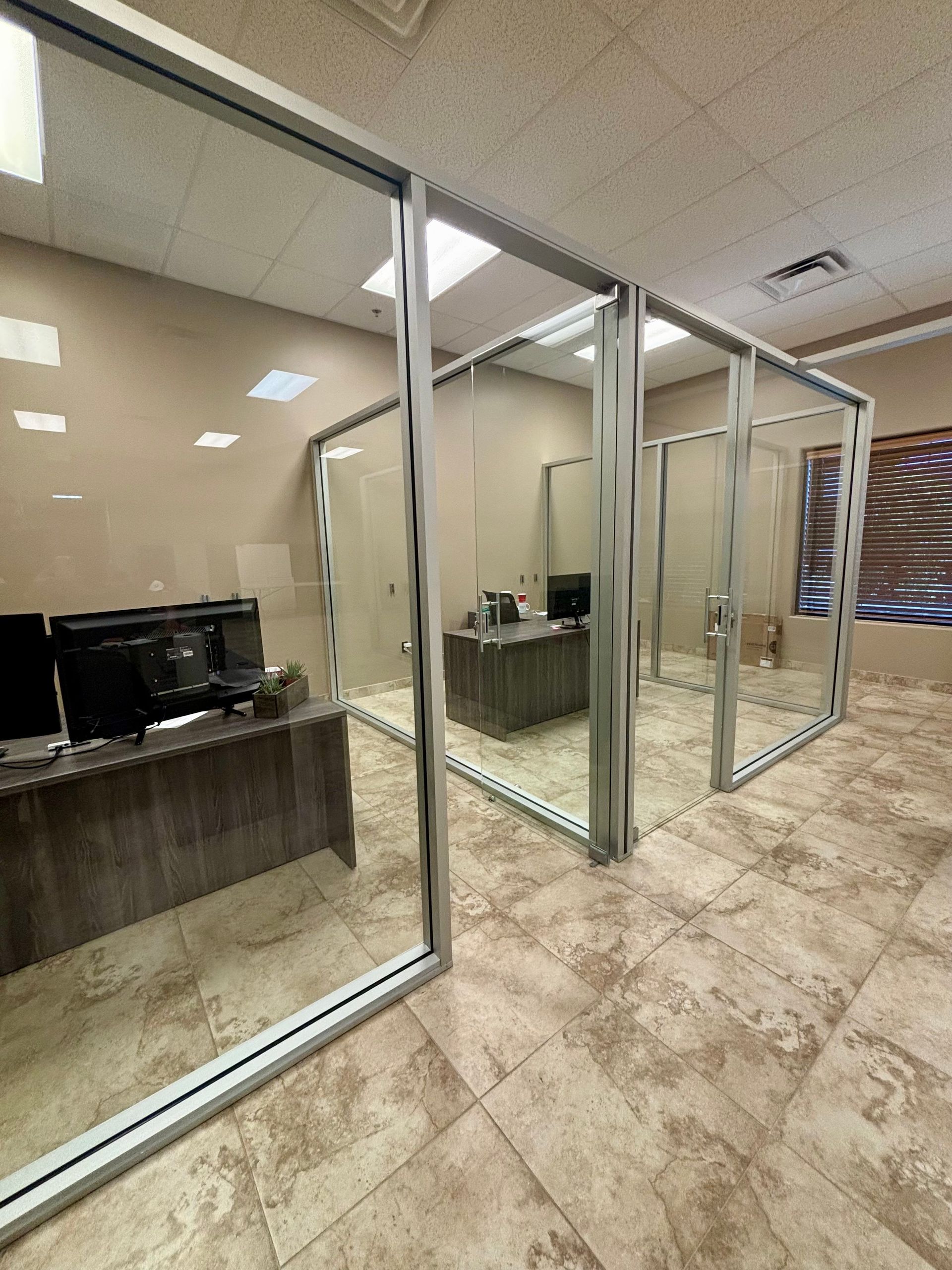 Office with glass walls, desk, computer monitors, and a tile floor.