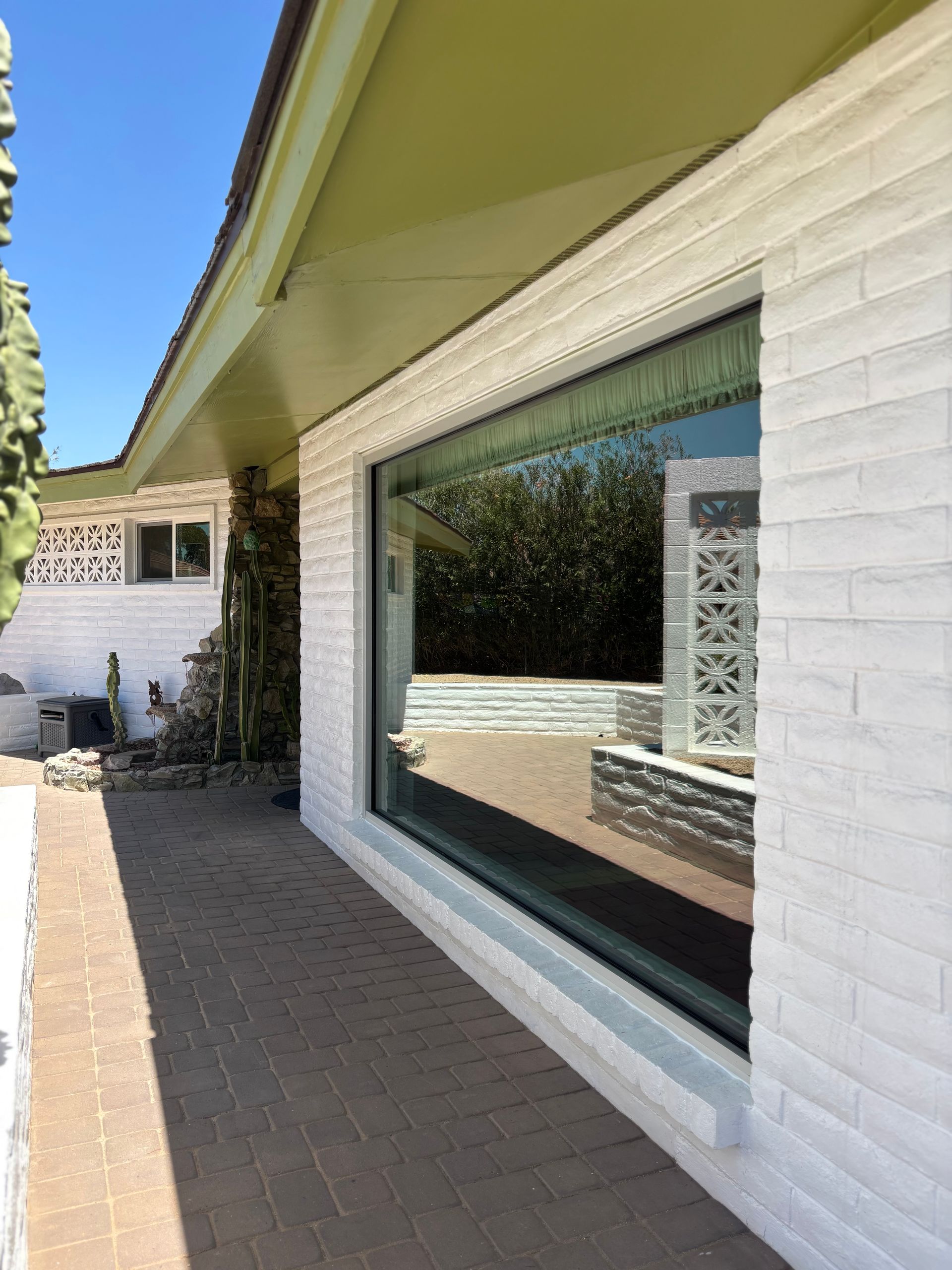 Long, rectangular window reflects an outdoor patio, framed by white brick and a green awning.