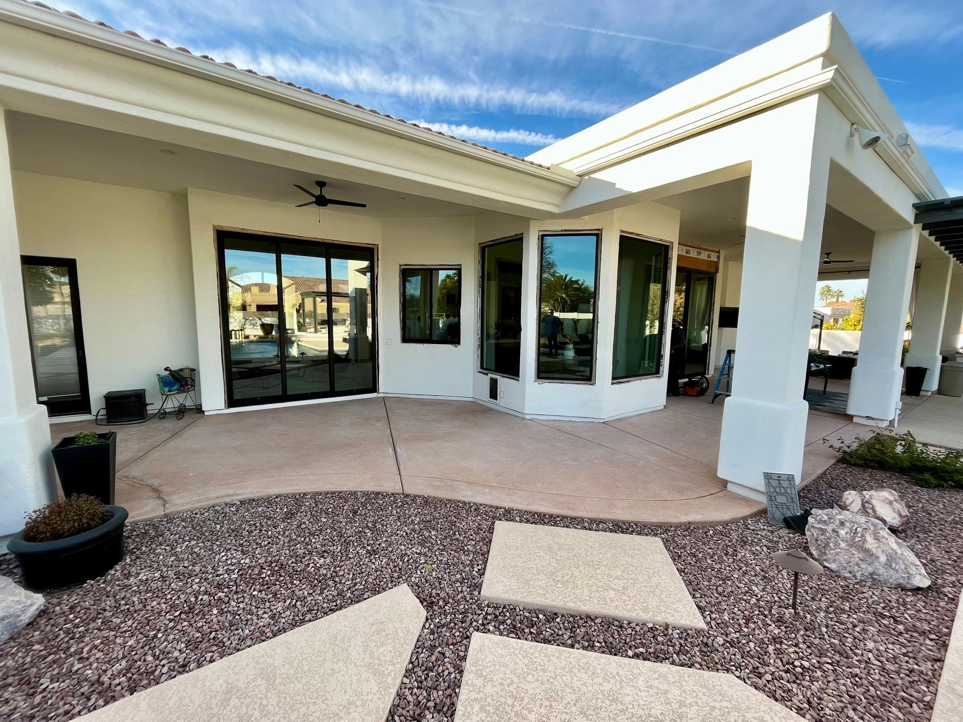 Patio with white pillars and sliding glass doors, surrounded by rock landscaping and stone pavers.