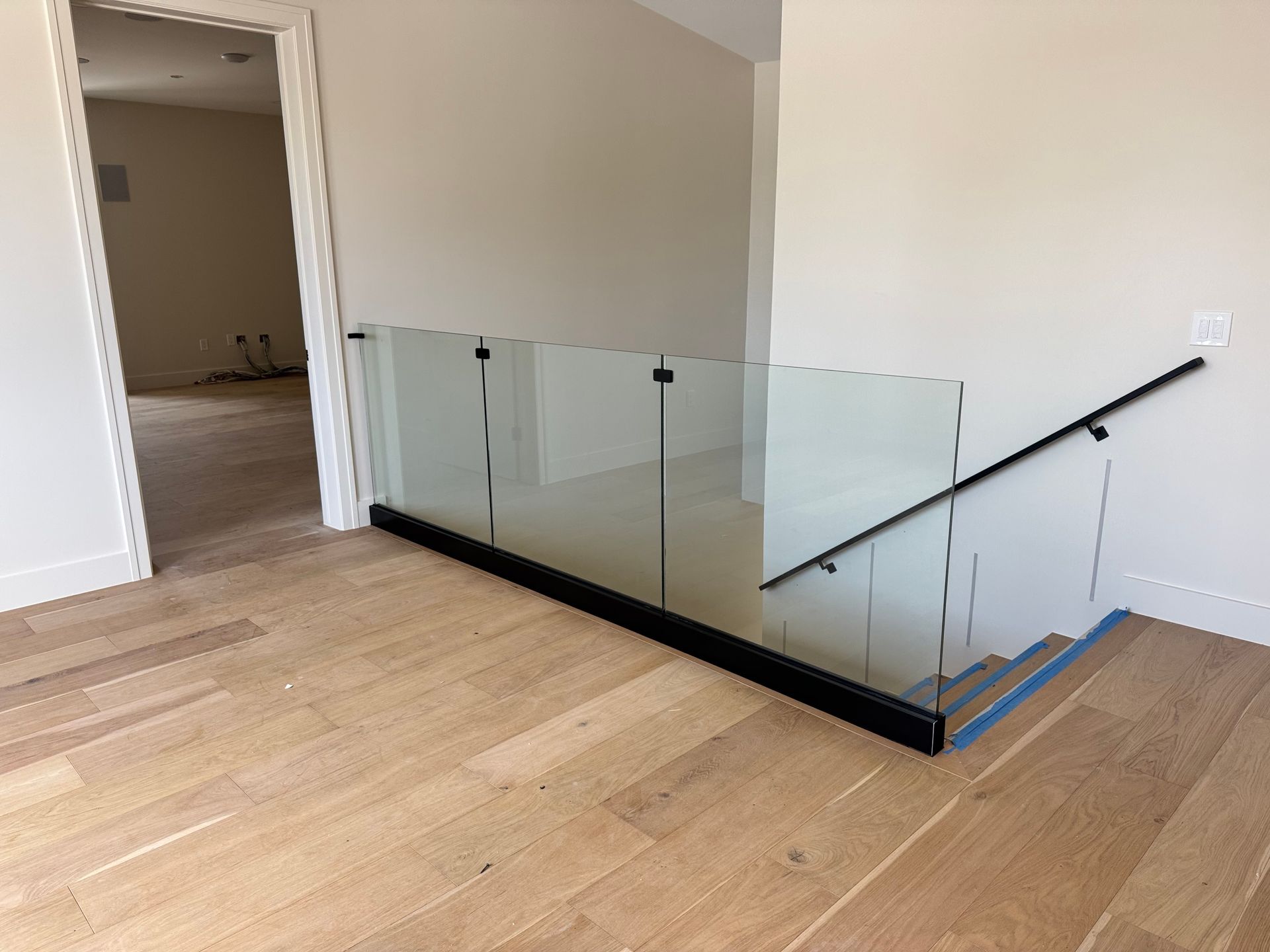 Wooden floor with glass railing and staircase. Black handrail. Light walls. Empty doorway.