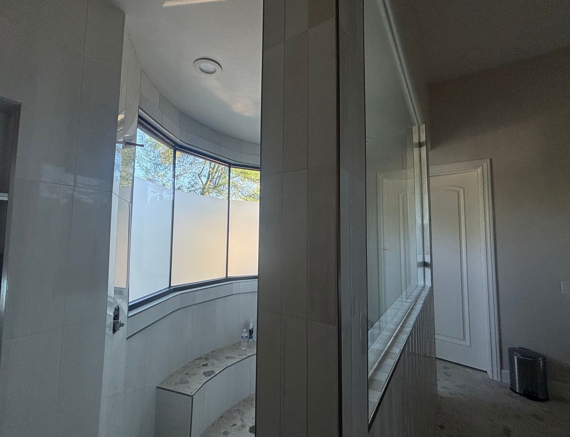 Bathroom with frosted windows, glass shower, and partially visible door. Gray and white tones dominate.