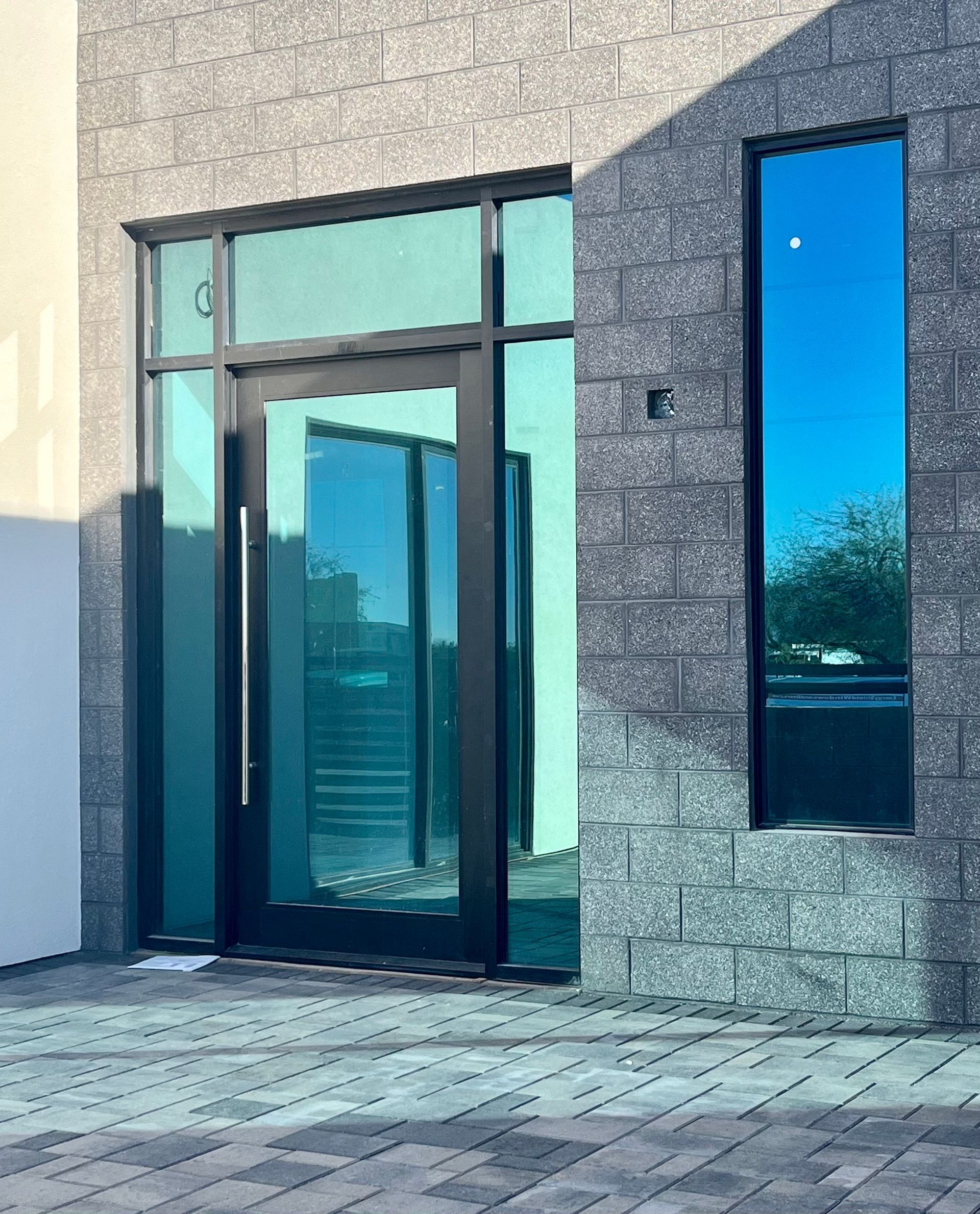 Modern entry with tinted glass door and matching tall window, set in gray stone brick.