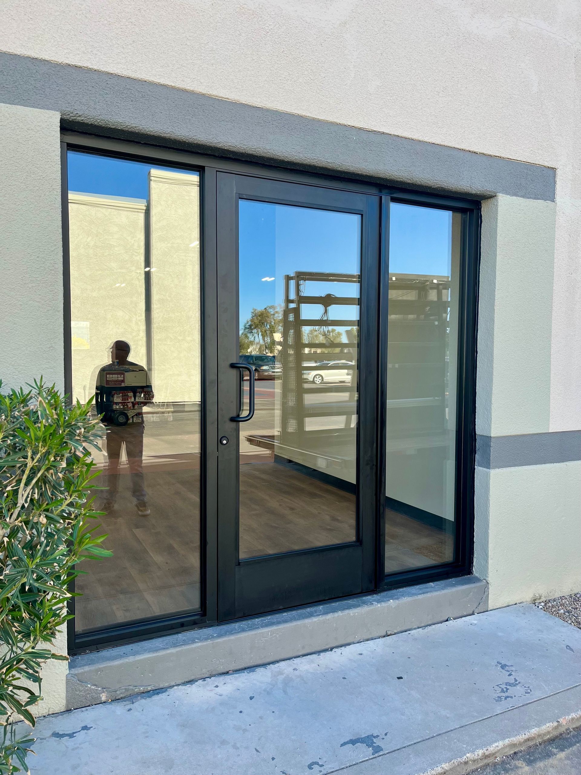 Black glass door and windows in a neutral-colored building, with a person reflected in the glass.