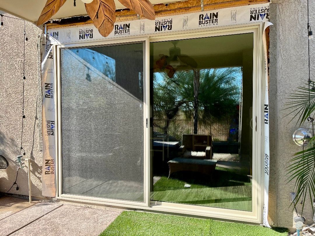 Sliding glass door, beige frame, exterior view; protective tape applied during installation.