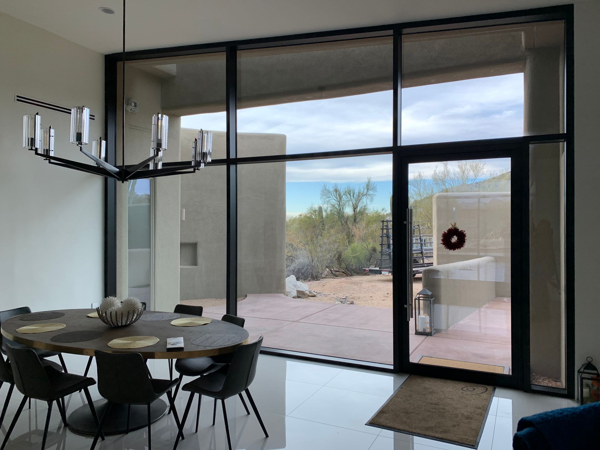 Dining room with large windows overlooking a desert landscape. Black chandelier, oval table, and chairs.