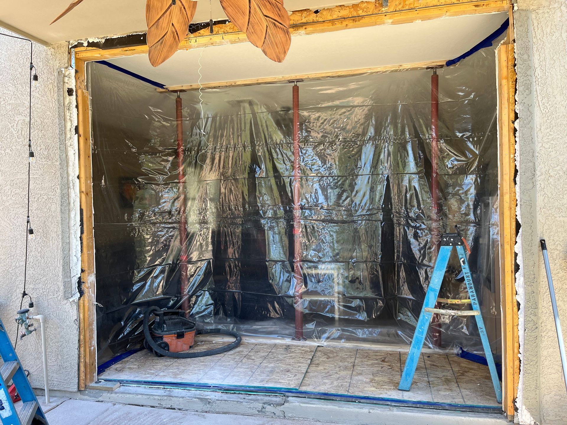 Construction site: doorway sealed with plastic sheeting, supports, ladder, vacuum.