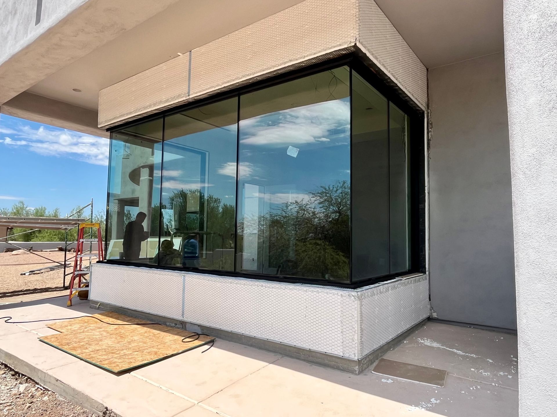 Glass-walled corner of a modern building under construction, with reflective windows and a textured concrete base.