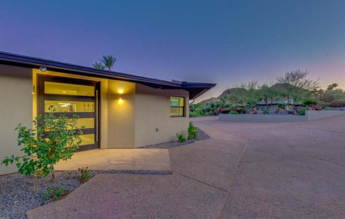 Modern home exterior with large glass door, tan walls, and desert landscaping.