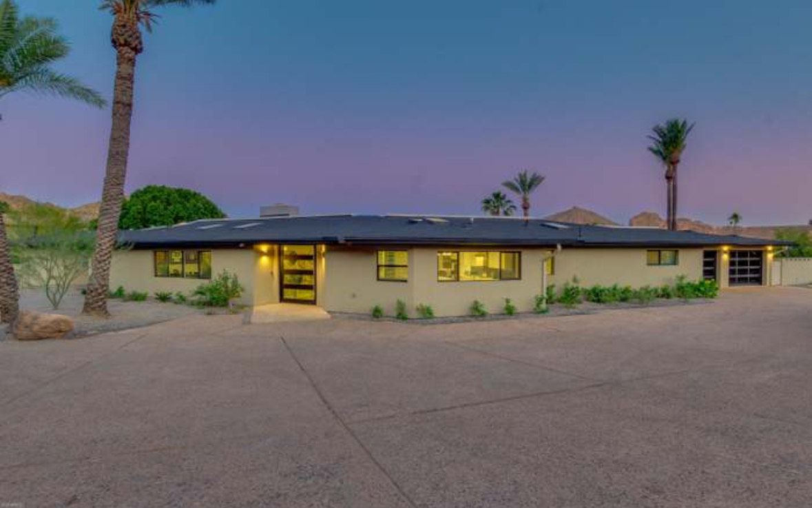 Beige modern home with palm trees and a dark sky at dusk.