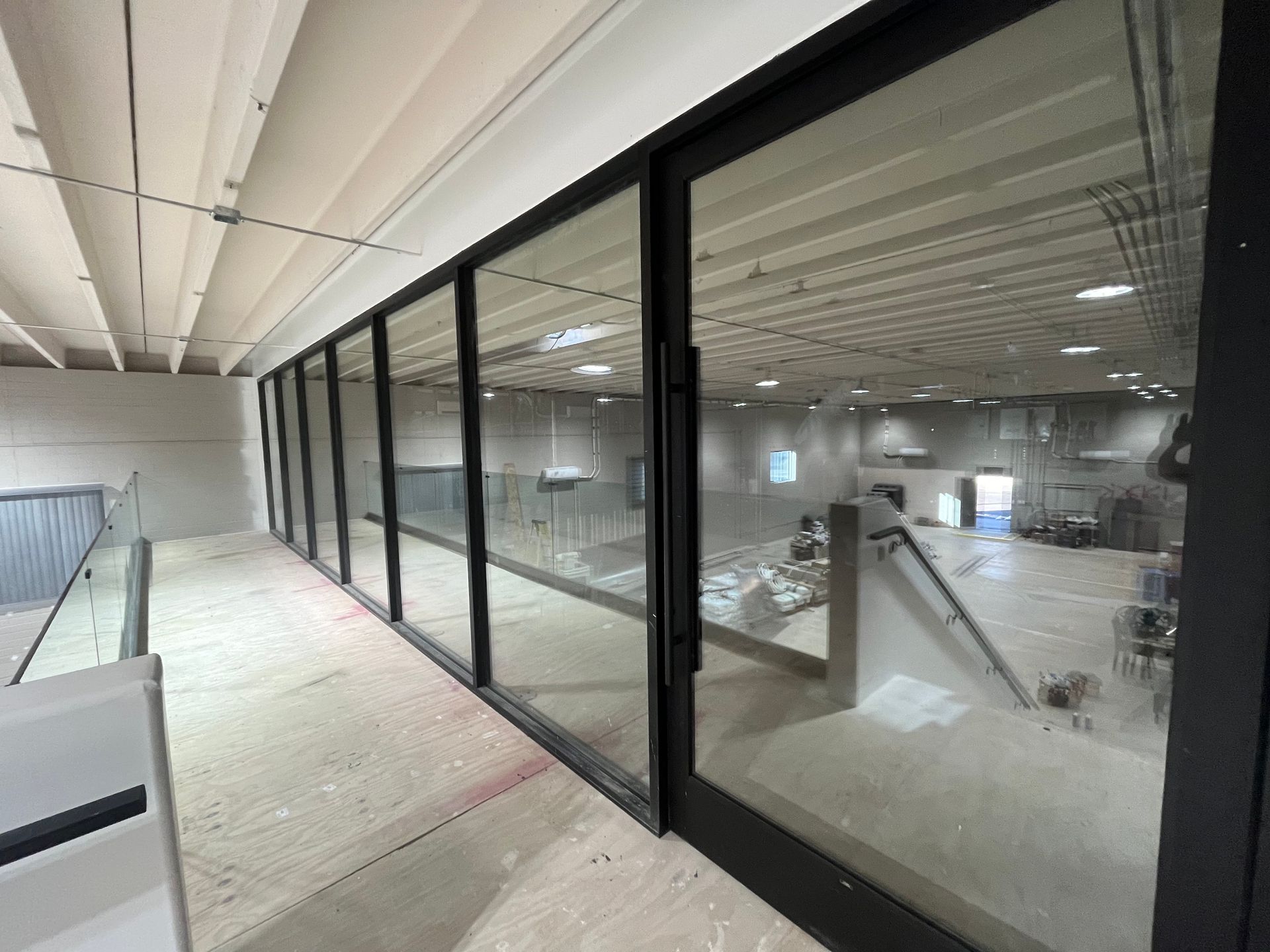 View through large glass doors into a large room; concrete floor, white ceiling, and some equipment.