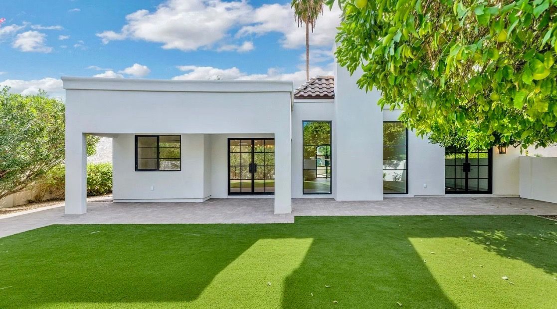 White modern house with black framed windows, green lawn, and blue sky.