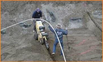 Two men are working on a tractor in the dirt.