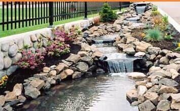 A waterfall is surrounded by rocks and flowers in a garden.
