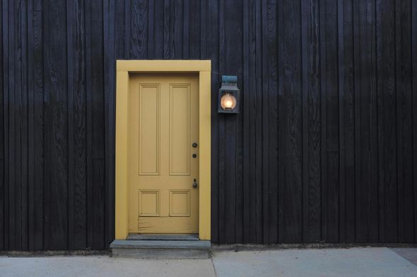 A yellow door is against a black wooden wall.