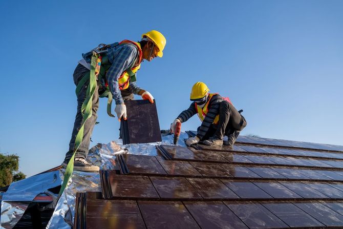 Roofers installing tiles on a residential house roof.