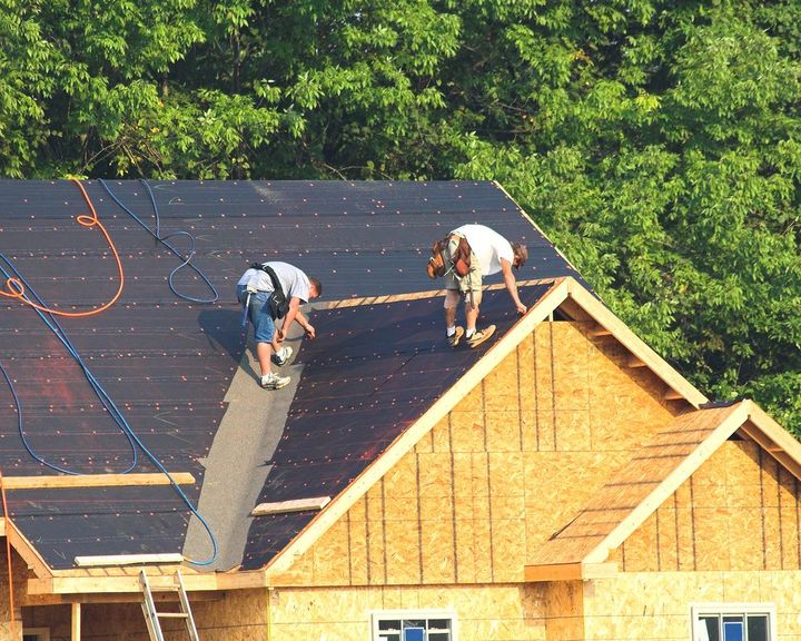 Two roofers installing black underlayment on a new house.