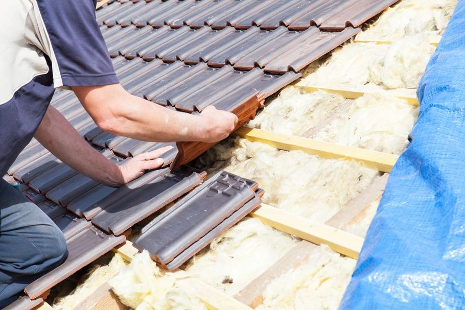 A worker installing brown roof tiles over yellow insulation material on a pitched roof.