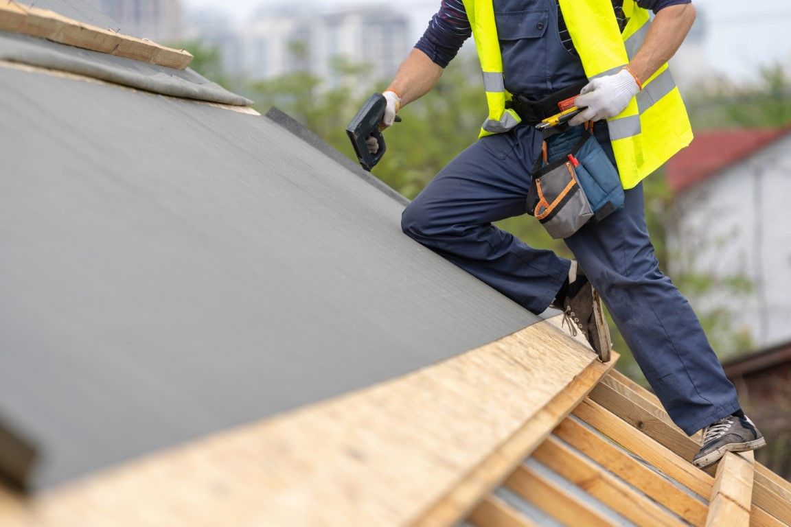 Roofer installing blue metal roofing with a power drill.