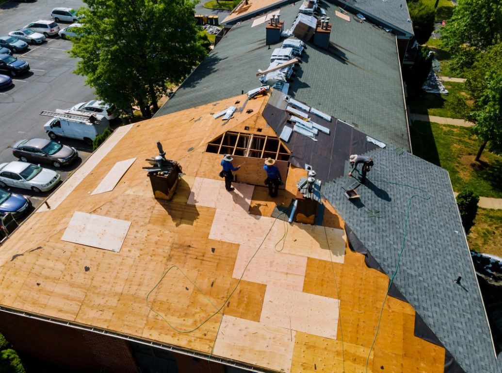 Two workers installing red metal roof tiles.