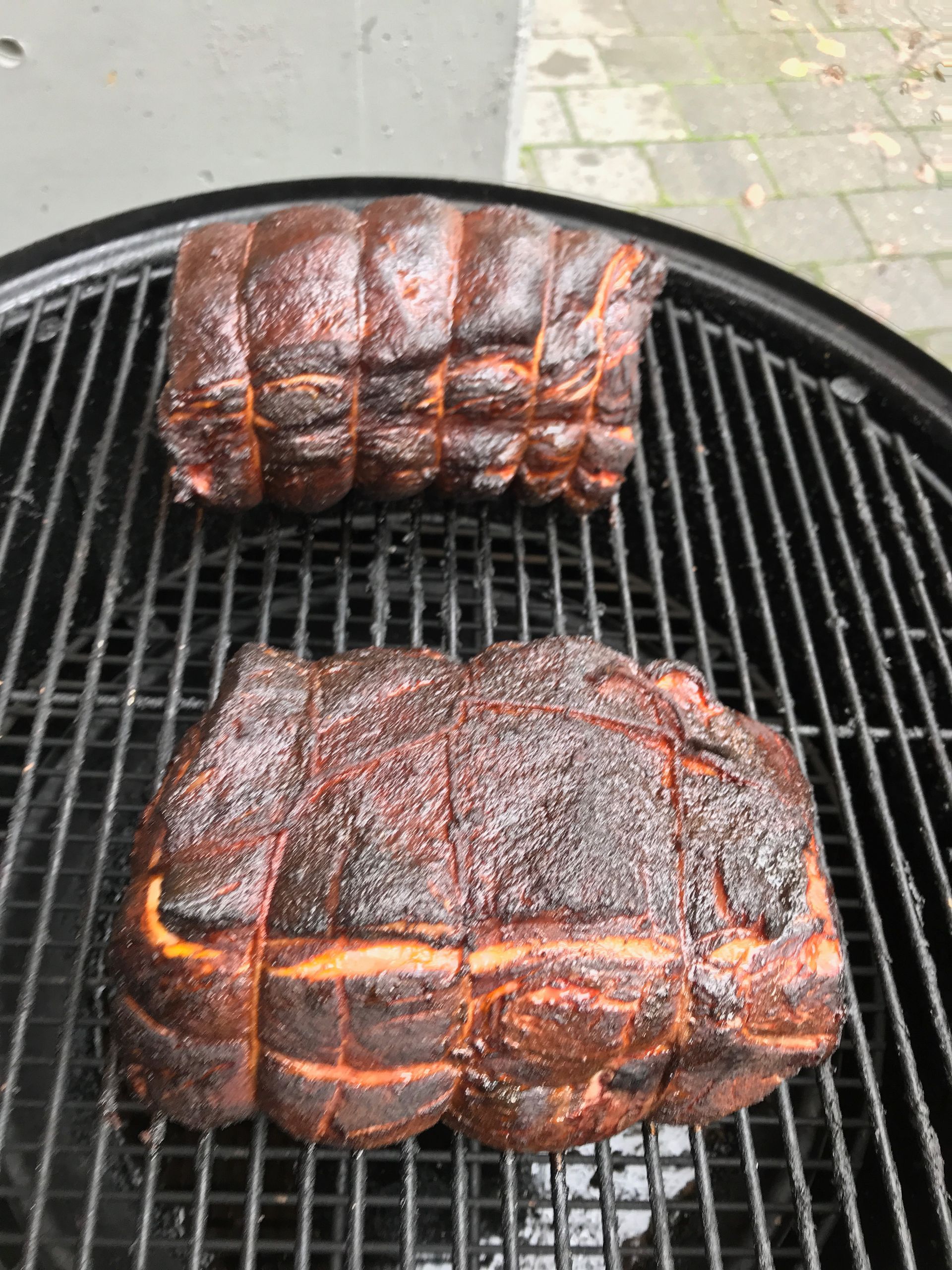 Two seasoned pork roasts on a black grill, looking charred and ready to cook.